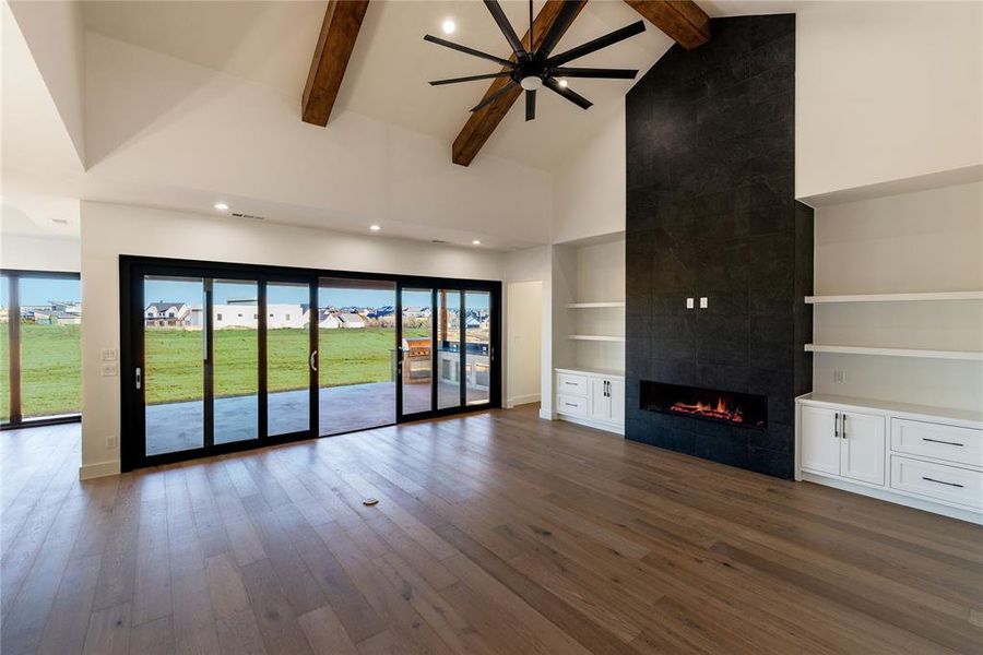 Unfurnished living room featuring dark wood-type flooring, high vaulted ceiling, a tile fireplace, and beamed ceiling