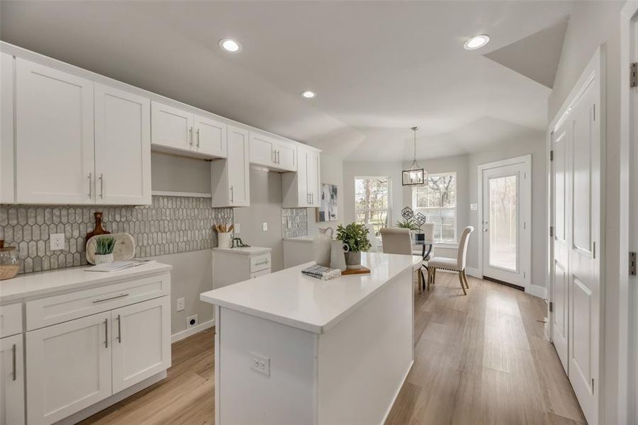 Kitchen with light hardwood / wood-style flooring, white cabinets, decorative light fixtures, a kitchen island, and decorative backsplash