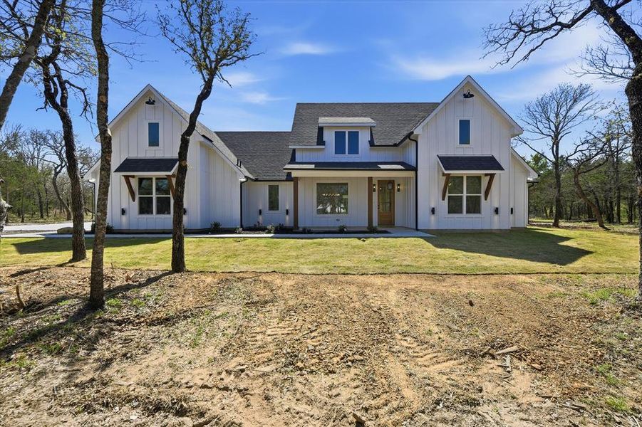 Modern farmhouse style home featuring board and batten siding, roof with shingles, a porch, and a front lawn