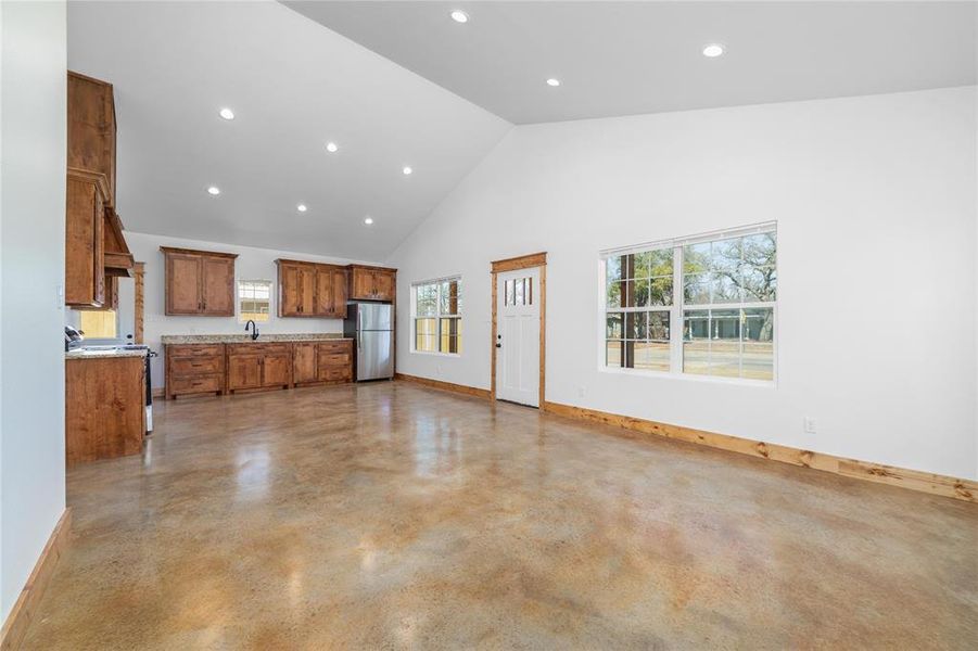 Kitchen featuring high vaulted ceiling, baseboards, range, freestanding refrigerator, and brown cabinets Kitchen featuring high vaulted ceiling, baseboards, range, freestanding refrigerator, and brown cabinets