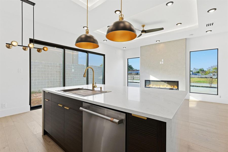 Same floorplan - different finishes. The oversized waterfall island features a built-in workstation sink, integrated dishwasher, and gold-tone hardware beneath designer pendant lighting.