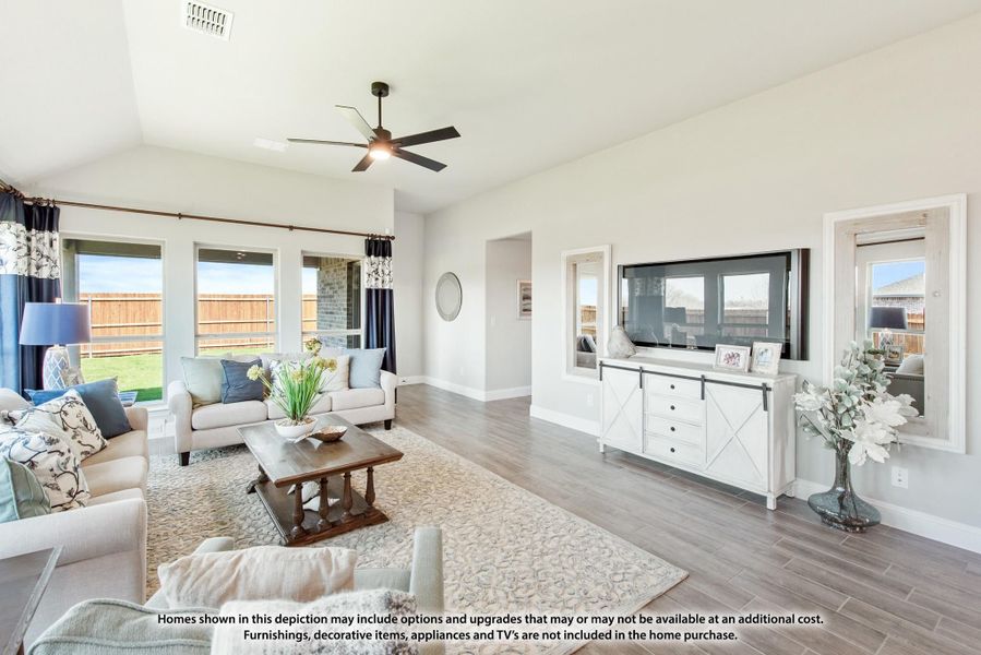 Bright living room with vaulted ceiling, ceiling fan, hardwood floors, and large windows overlooking backyard