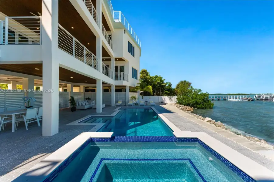 Multi-level exterior featuring tiered balconies with metal railings, a covered patio with recessed lighting, an integrated swimming pool and spa, and bulkhead waterfront access Multi-level exterior featuring tiered balconies with metal railings, a covered patio with recessed lighting, an integrated swimming pool and spa, and bulkhead waterfront access