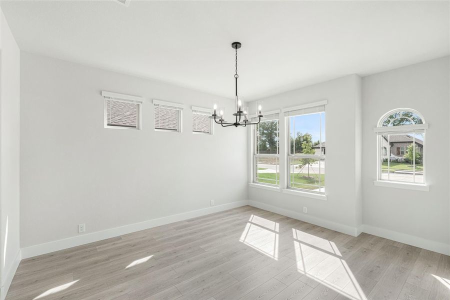 Empty dining room with black chandelier, light wood floors, and large windows with natural light