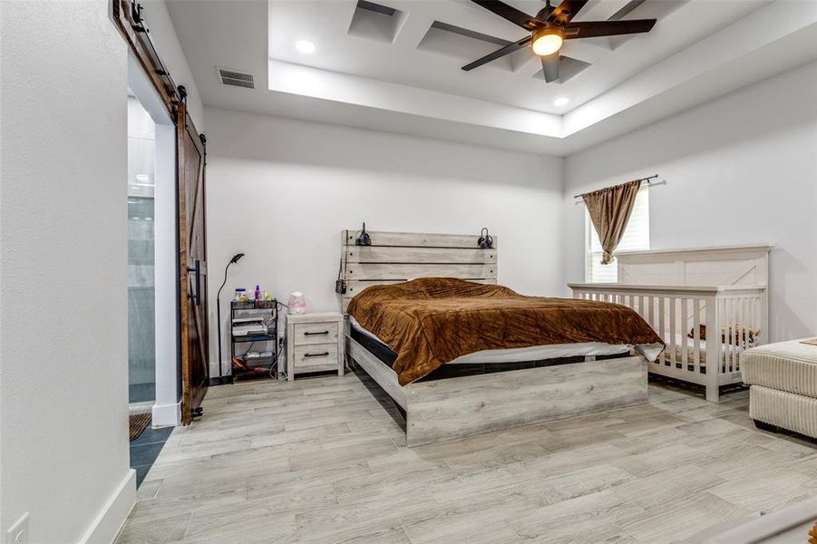 Bedroom with a barn door, visible vents, baseboards, light wood-style flooring, and recessed lighting