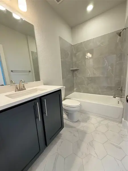 Full bath with vanity, bathing tub / shower combination, toilet, a textured wall, and marble finish floor