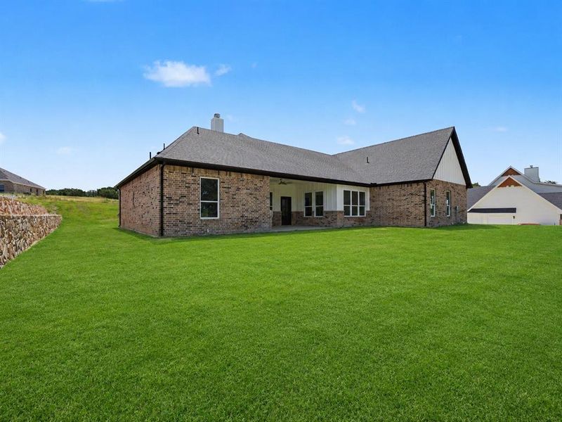 Expansive rear lawn featuring a brick and siding exterior, covered patio, and dark shingle roof