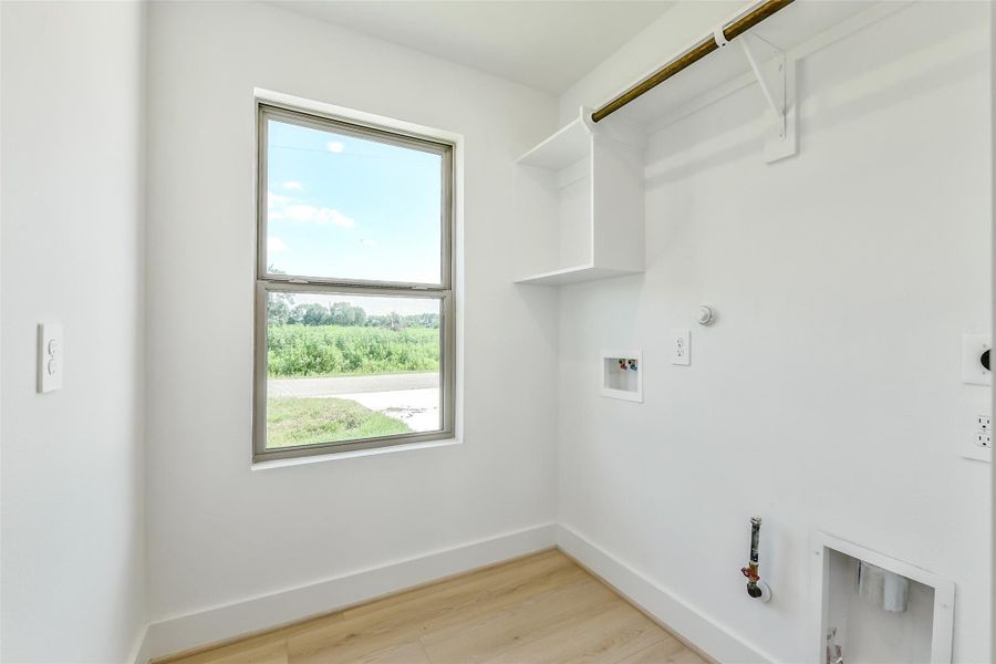 Bright laundry room with hanging space, upper shelving and a window that brings in natural light and views of the corner lot.