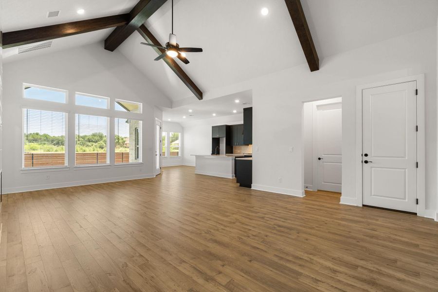 A spacious living area features high vaulted ceilings with exposed beams and abundant natural light from large windows.