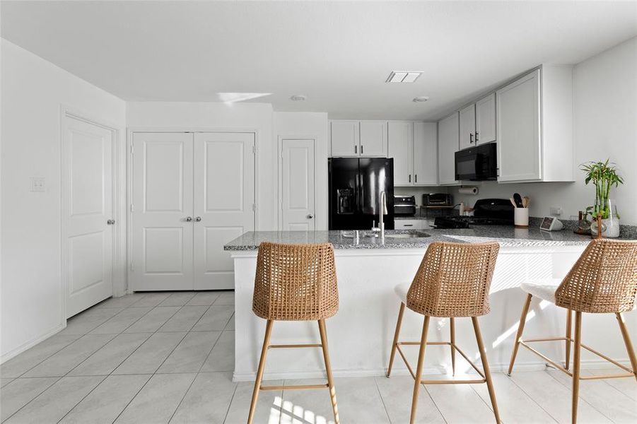 Kitchen with a peninsula, a breakfast bar area, light stone counters, light tile patterned floors, and black appliances