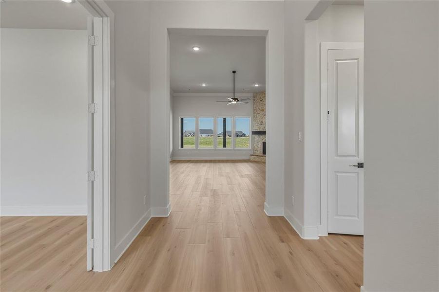 Light wood-finish flooring extending into an open living area featuring a stone fireplace, large windows, and a ceiling fan Light wood-finish flooring extending into an open living area featuring a stone fireplace, large windows, and a ceiling fan