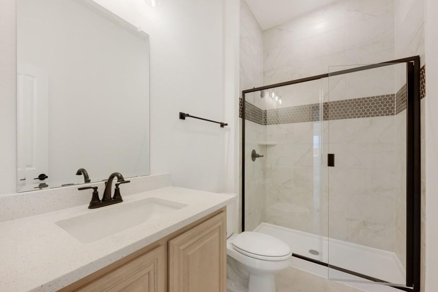 Bathroom with quartz vanity, glass-enclosed walk-in shower with marble tile, and dark bronze fixtures