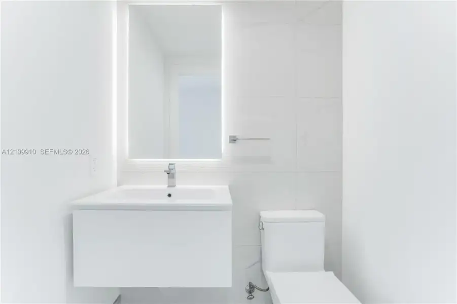 Modern floating vanity with a seamless sink, LED-backlit mirror, and large-format porcelain tile wall cladding