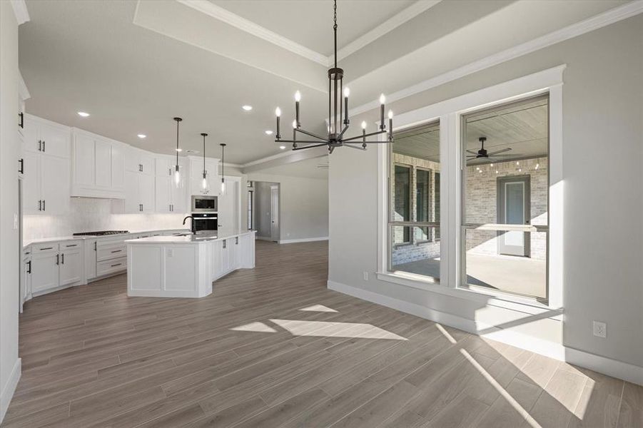 Kitchen with decorative light fixtures, ceiling fan with notable chandelier, an island with sink, and door to patio.