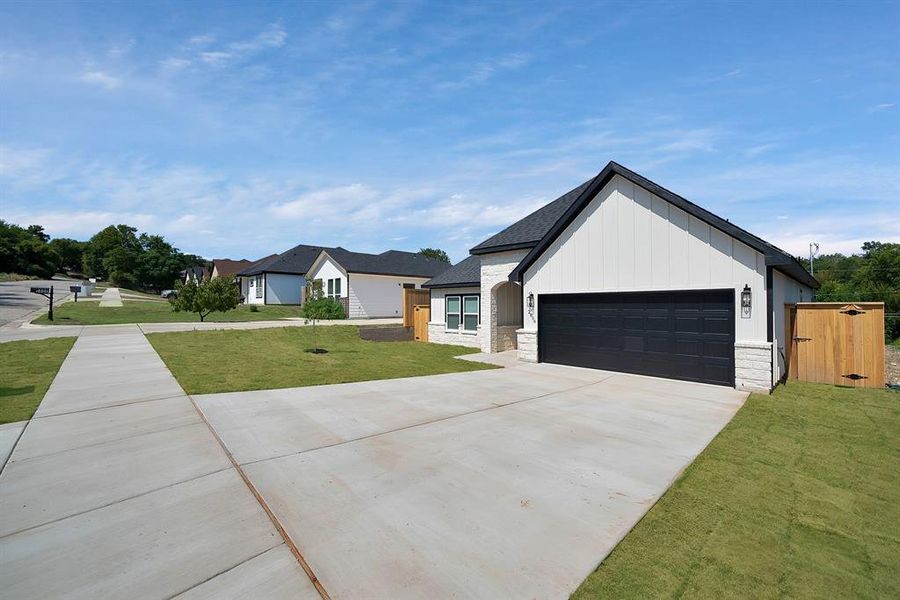 Modern farmhouse featuring stone siding, concrete driveway, an attached garage, and a front yard Modern farmhouse featuring stone siding, concrete driveway, an attached garage, and a front yard
