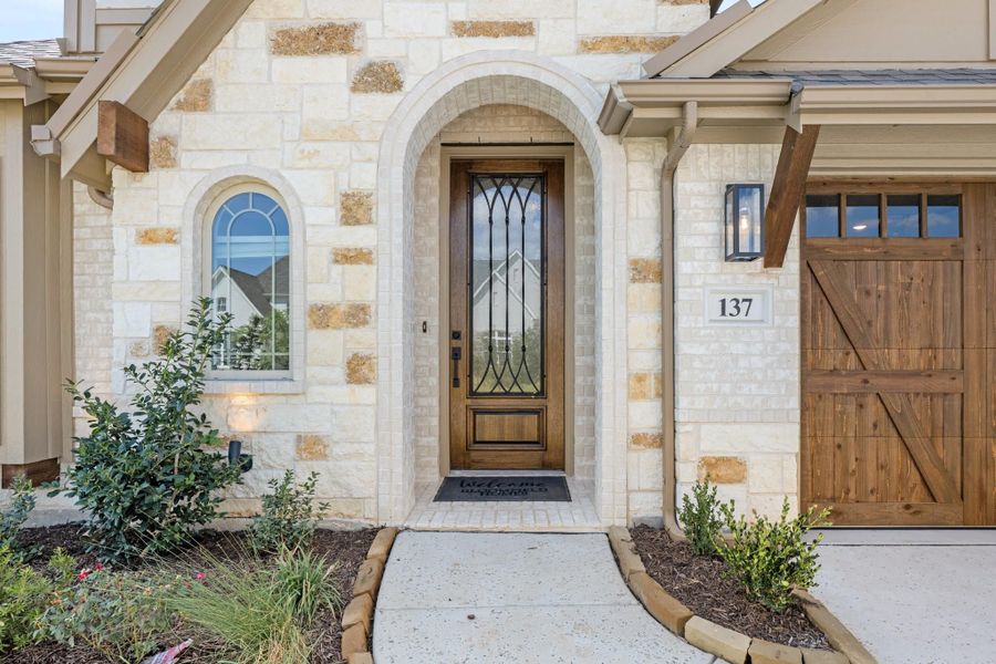 Stone home entrance with arched doorway, wood and iron front door, and wood garage door beside landscaped walkway