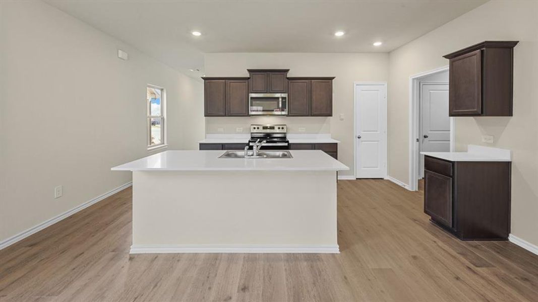 Contemporary kitchen featuring an expansive center island with an undermount sink, dark wood cabinetry, white countertops, and wood-finish flooring
