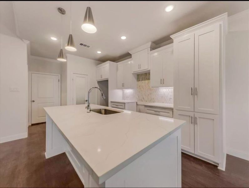 Kitchen featuring light stone countertops, hanging light fixtures, white cabinets, an island with sink, and ornamental molding Kitchen featuring light stone countertops, hanging light fixtures, white cabinets, an island with sink, and ornamental molding