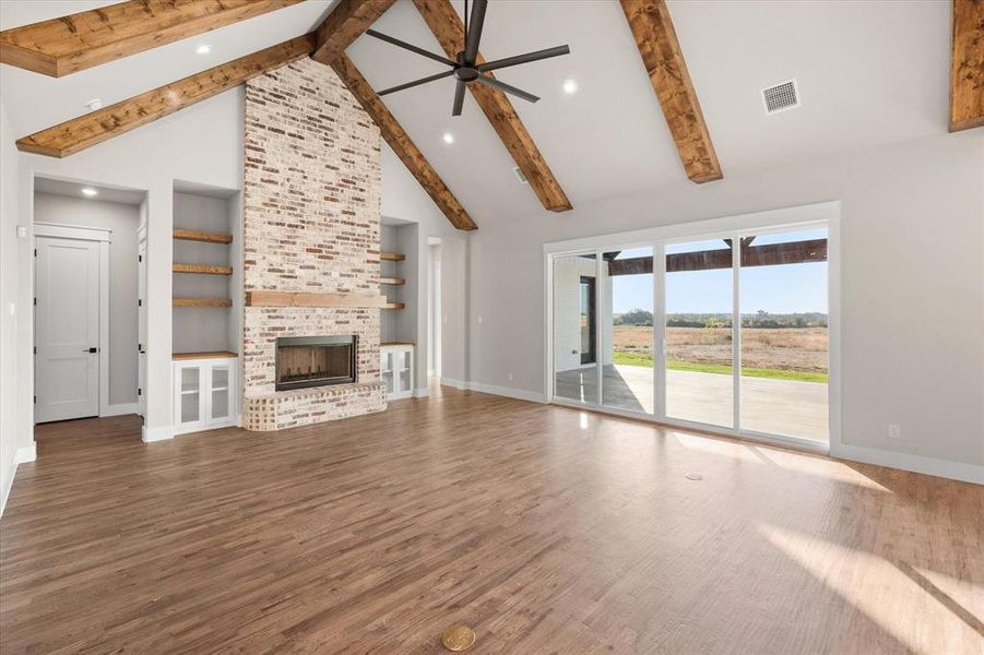 Unfurnished living room featuring beam ceiling, hardwood / wood-style flooring, high vaulted ceiling, and a brick fireplace