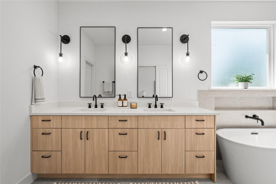 The primary bathroom features a large double vanity with wood cabinets, matte black pulls, and a white quartz countertop with dual under-mount sinks. Two black-framed mirrors are flanked by globe sconces, and a deep freestanding soaking tub sits right under a frosted privacy window.