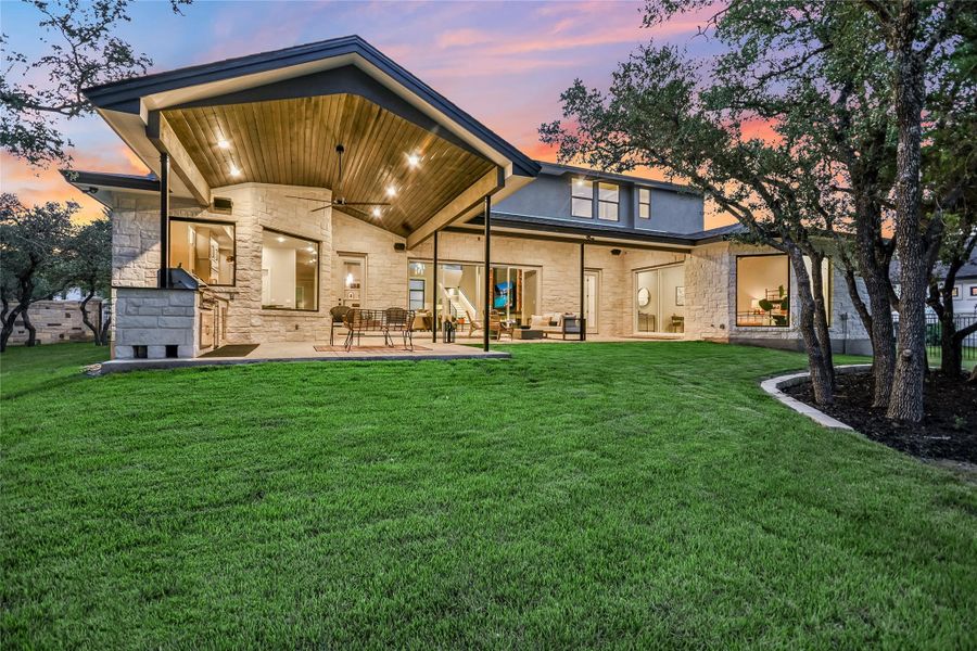 Back of property at dusk featuring stone siding, a patio area, and a lawn Back of property at dusk featuring stone siding, a patio area, and a lawn