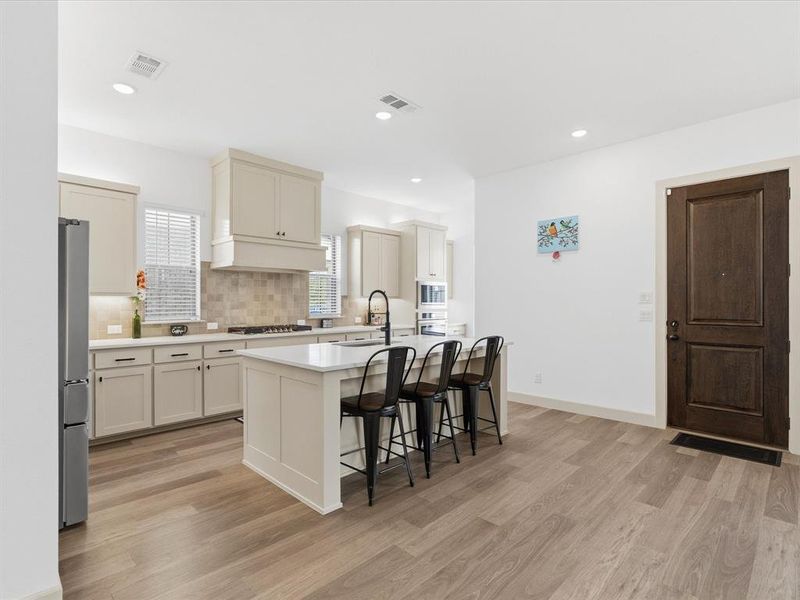 Spacious kitchen featuring a central island with countertop seating, light-toned cabinetry, light wood-finish flooring, recessed lighting, and a tile backsplash