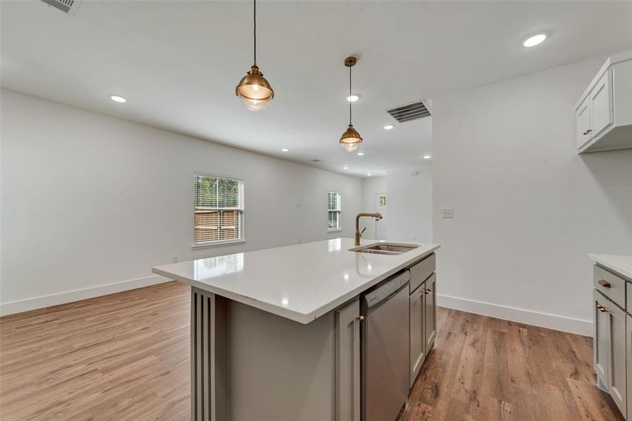 Kitchen featuring hanging light fixtures, stainless steel dishwasher, a center island with sink, light wood-style floors, and recessed lighting Kitchen featuring hanging light fixtures, stainless steel dishwasher, a center island with sink, light wood-style floors, and recessed lighting