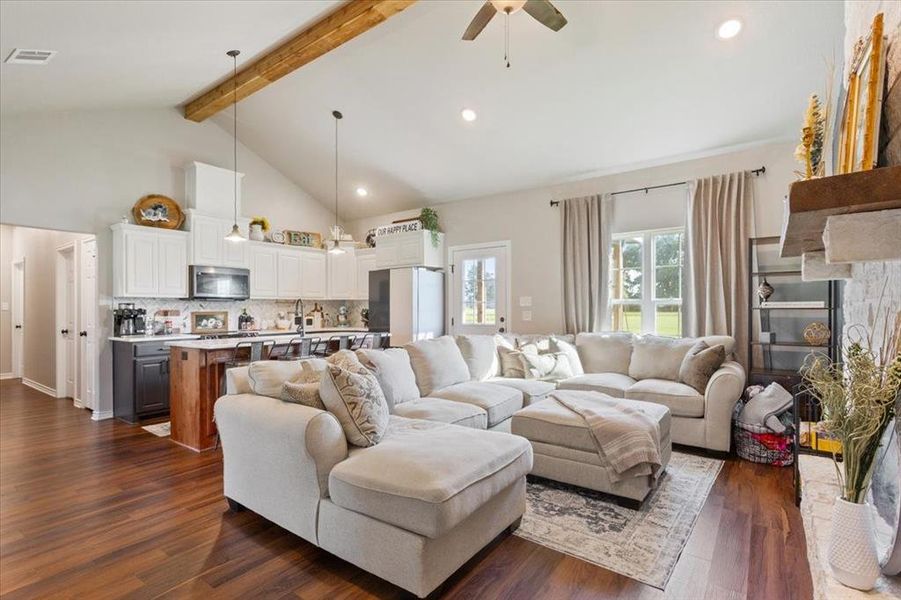 Living area with beamed ceiling, dark wood finished floors, high vaulted ceiling, a ceiling fan, and a stone fireplace