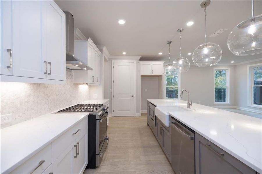 Kitchen featuring sink, white cabinets, hanging light fixtures, stainless steel appliances, and wall chimney exhaust hood