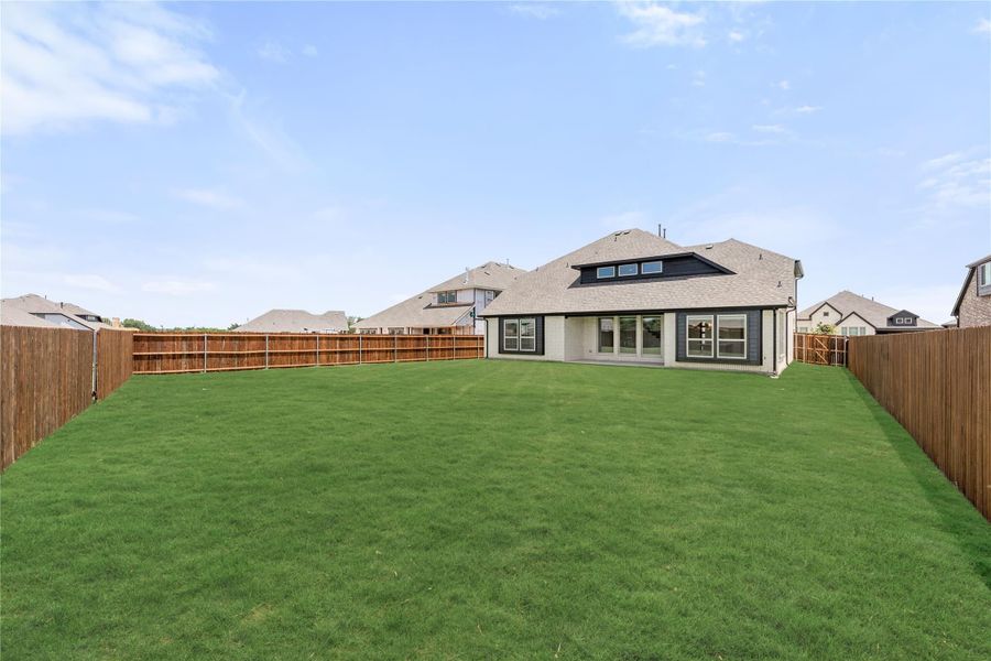 Large fenced backyard with green lawn and rear view of two-story home with patio doors