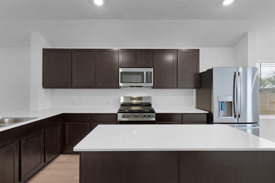 Kitchen with dark brown cabinetry, appliances with stainless steel finishes, tasteful backsplash, a kitchen island, and recessed lighting Kitchen with dark brown cabinetry, appliances with stainless steel finishes, tasteful backsplash, a kitchen island, and recessed lighting