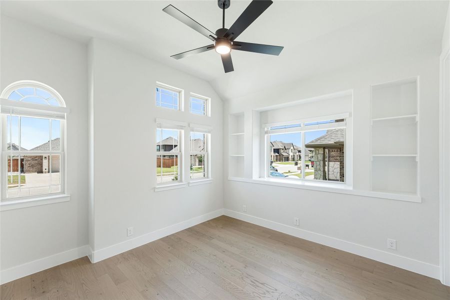 Empty room with vaulted ceiling, ceiling fan, built-in shelves, and light hardwood floors Empty room with vaulted ceiling, ceiling fan, built-in shelves, and light hardwood floors
