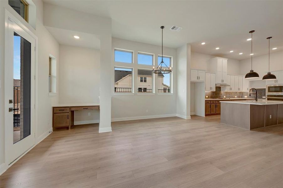Two tone kitchen featuring built in desk, backsplash, an island with sink, two tone cabinetry, and light wood finished floors