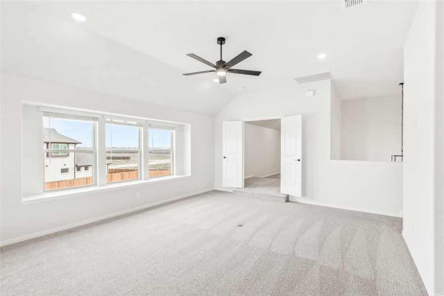 Spacious empty bedroom with vaulted ceiling, ceiling fan, gray carpet, and large windows overlooking neighboring homes. Spacious empty bedroom with vaulted ceiling, ceiling fan, gray carpet, and large windows overlooking neighboring homes.