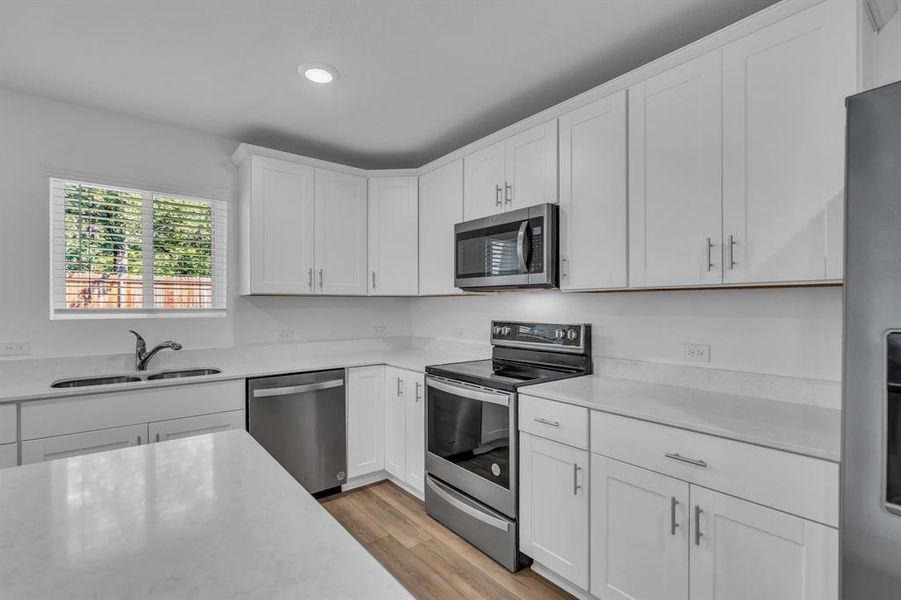 Kitchen featuring stainless steel appliances, white cabinets, light wood-style flooring, recessed lighting, and light stone countertops
