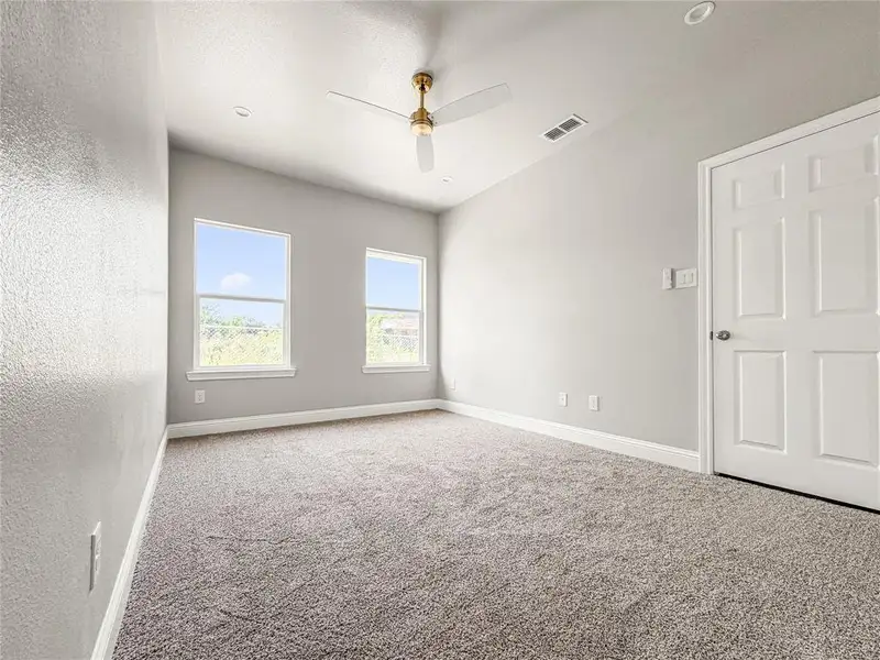 Light-filled room featuring two windows, neutral tone carpeting, a ceiling fan with integrated lighting, recessed lighting, and a paneled interior door Light-filled room featuring two windows, neutral tone carpeting, a ceiling fan with integrated lighting, recessed lighting, and a paneled interior door