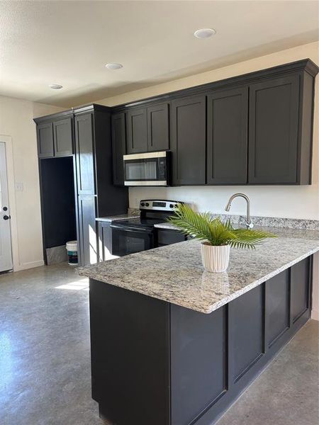 Kitchen featuring kitchen peninsula, light stone counters, and stainless steel range