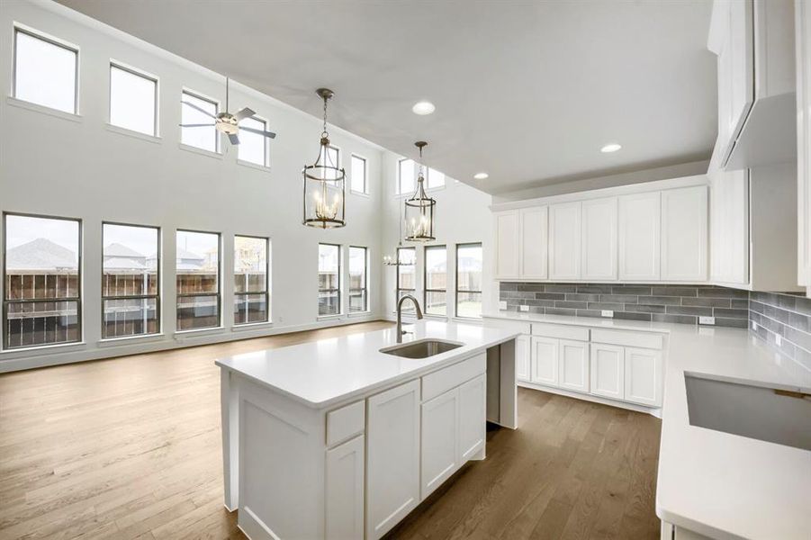 Modern kitchen featuring a central island with an undermount sink, white shaker cabinetry, light-toned countertops, and a gray subway tile backsplash Modern kitchen featuring a central island with an undermount sink, white shaker cabinetry, light-toned countertops, and a gray subway tile backsplash