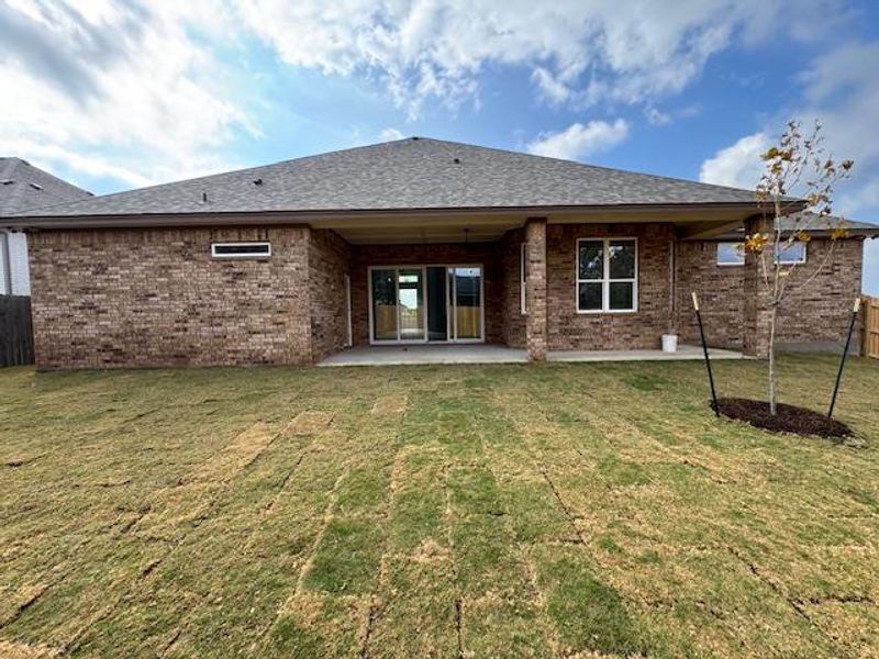 Back of property featuring brick siding, a patio, and roof with shingles