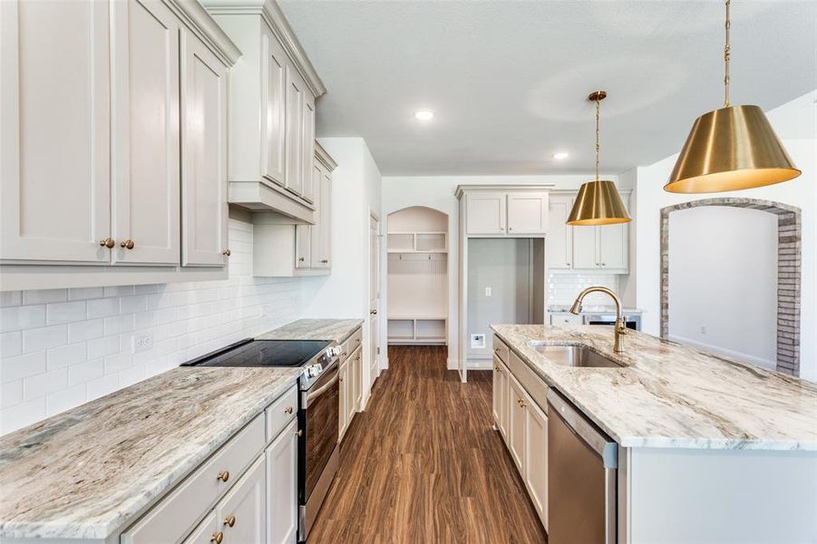 Kitchen featuring sink, light stone counters, appliances with stainless steel finishes, dark wood-type flooring, and pendant lighting