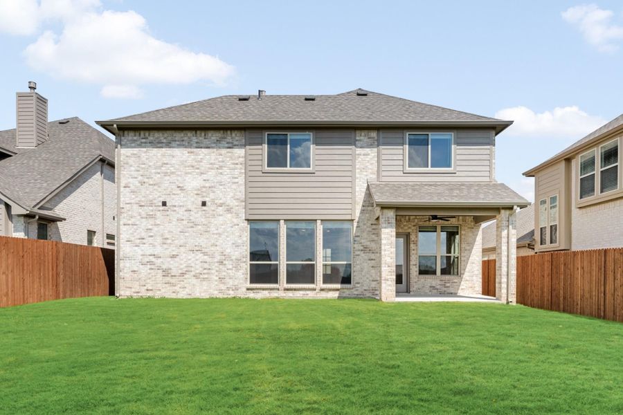 Two-story brick home rear exterior with covered patio, large windows, and fenced green backyard