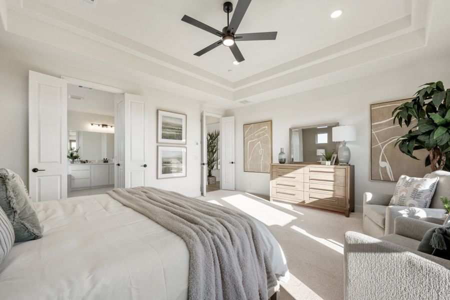 Master bedroom with tray ceiling, ceiling fan, and ensuite bathroom access