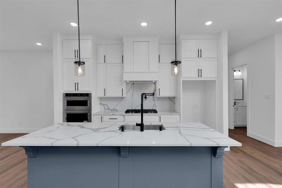 Kitchen featuring double oven, white cabinets, an island with sink, recessed lighting, and light wood-style flooring Kitchen featuring double oven, white cabinets, an island with sink, recessed lighting, and light wood-style flooring