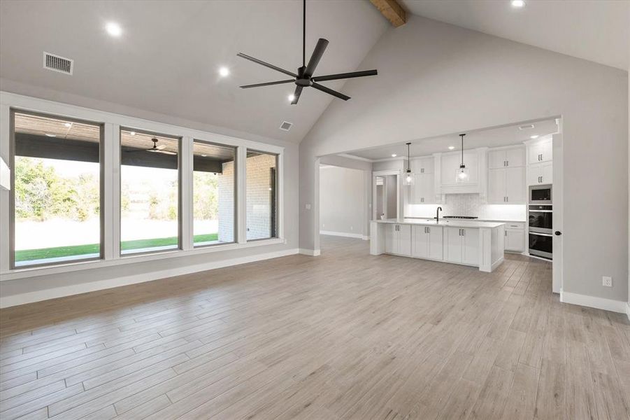 Unfurnished living room featuring sink, light wood-type flooring, ceiling fan, beam ceiling, and high vaulted ceiling