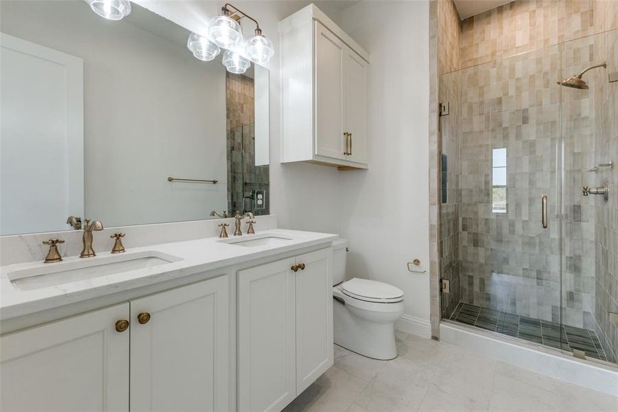 Bathroom featuring a shower stall, toilet, double vanity, baseboards, and marble finish floors