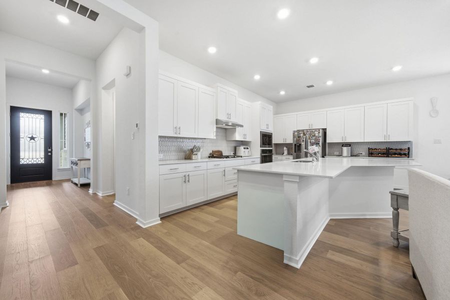 Kitchen with white cabinetry, a kitchen island with sink, tasteful backsplash, a breakfast bar, and light wood-type flooring