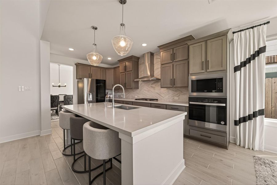 This modern kitchen features sleek cabinetry, quartz countertops, a large island with seating, stainless steel appliances, and elegant pendant lighting. The open layout flows into a dining area, creating an inviting space for entertaining.