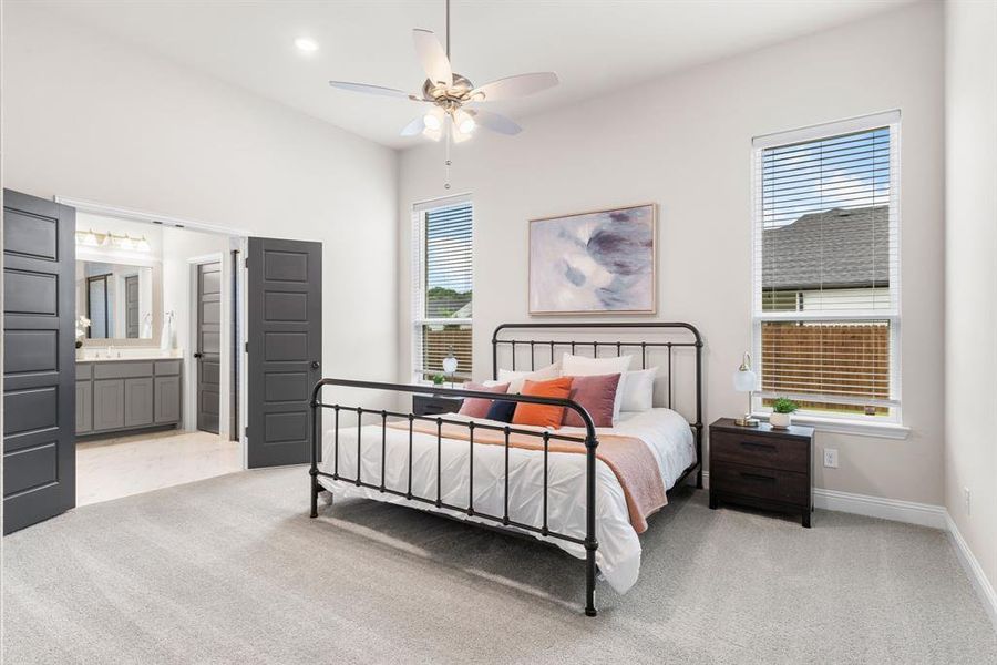 Carpeted bedroom with multiple windows, connected bathroom, and ceiling fan