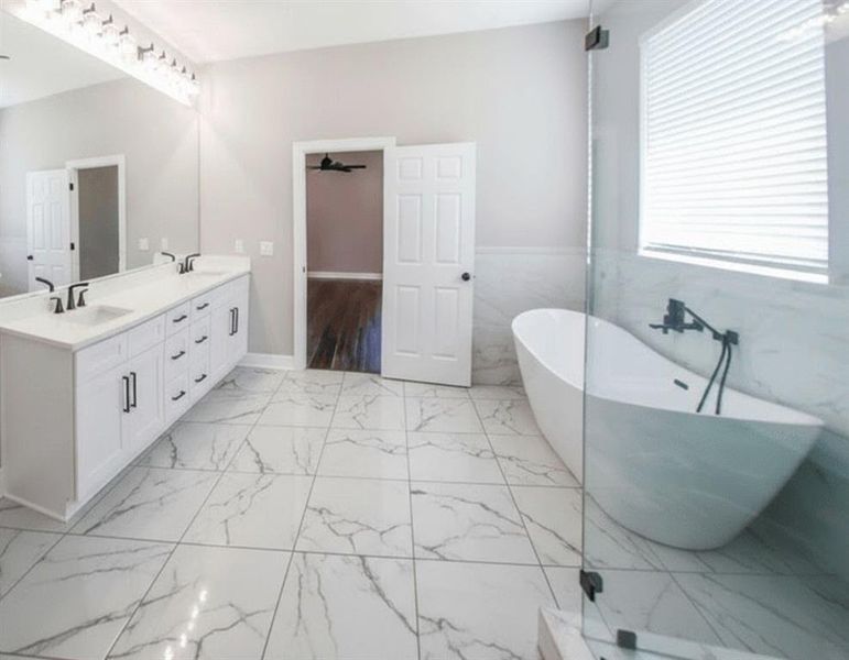 Bathroom featuring a soaking tub, double vanity, light marble finish flooring, and tile walls Bathroom featuring a soaking tub, double vanity, light marble finish flooring, and tile walls