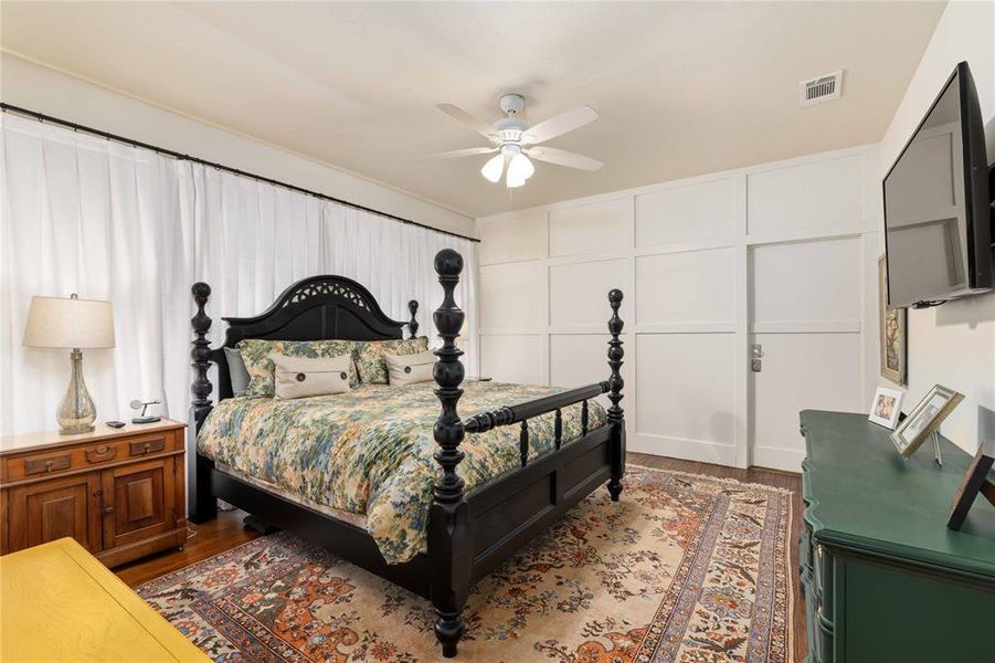 Bedroom featuring dark wood-finish flooring, white ceiling fan, and panel molding accent wall